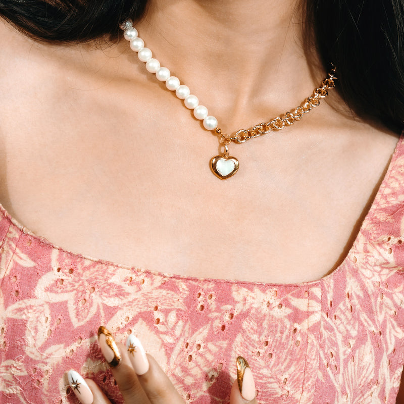 Woman wearing a pearl necklace with a heart charm on a light blue background