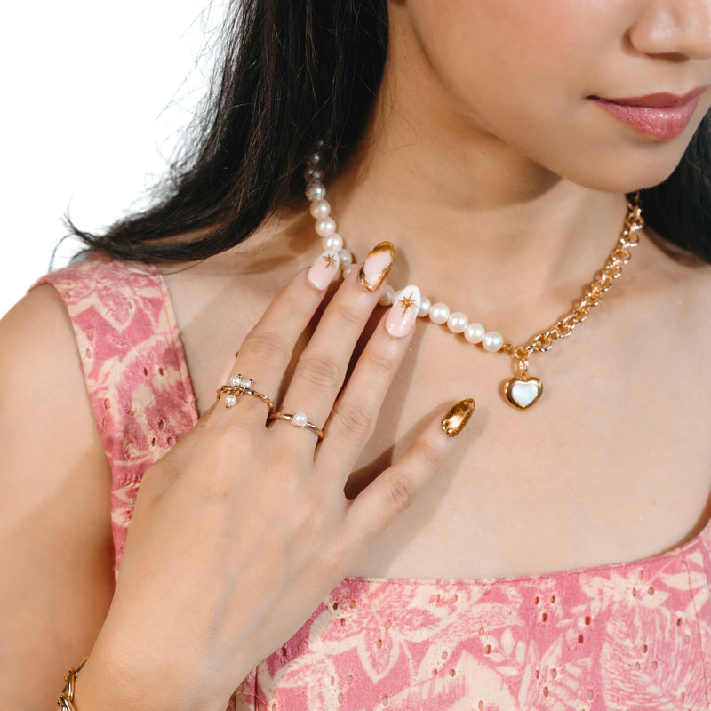 Woman wearing a gold necklace with a heart pendant, pearl bracelet, and ring on a white background